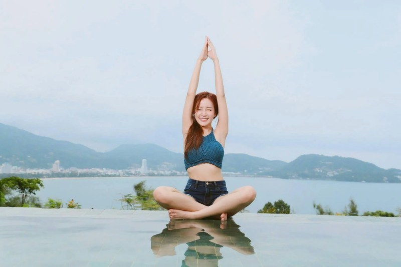 바다를 배경으로 양팔을 머리 위로 모으고 책상다리로 앉은 여성