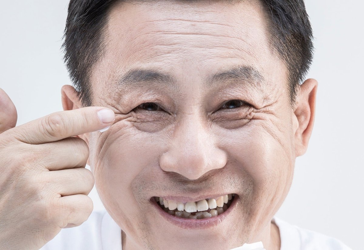 손가락으로 눈가 주름을 가리키며 웃는 중년 남성