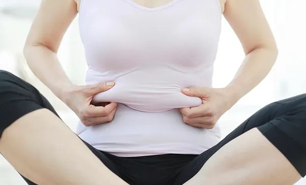 양손으로 뱃살을 잡고 앉아 있는 여성의 상체