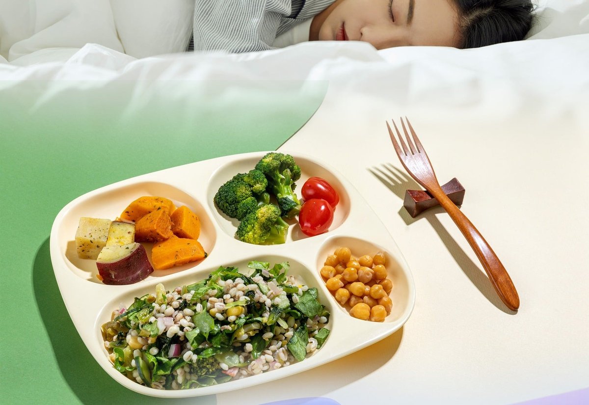 잠든 여성과 고구마·브로콜리·방울토마토·병아리콩·잡곡 샐러드가 담긴 식판, 나무 포크