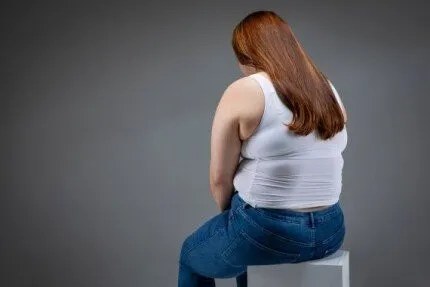 회색 배경 앞 의자에 등을 보이고 앉은 여성