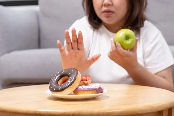 도넛 접시를 손으로 밀어내며 사과를 든 여성