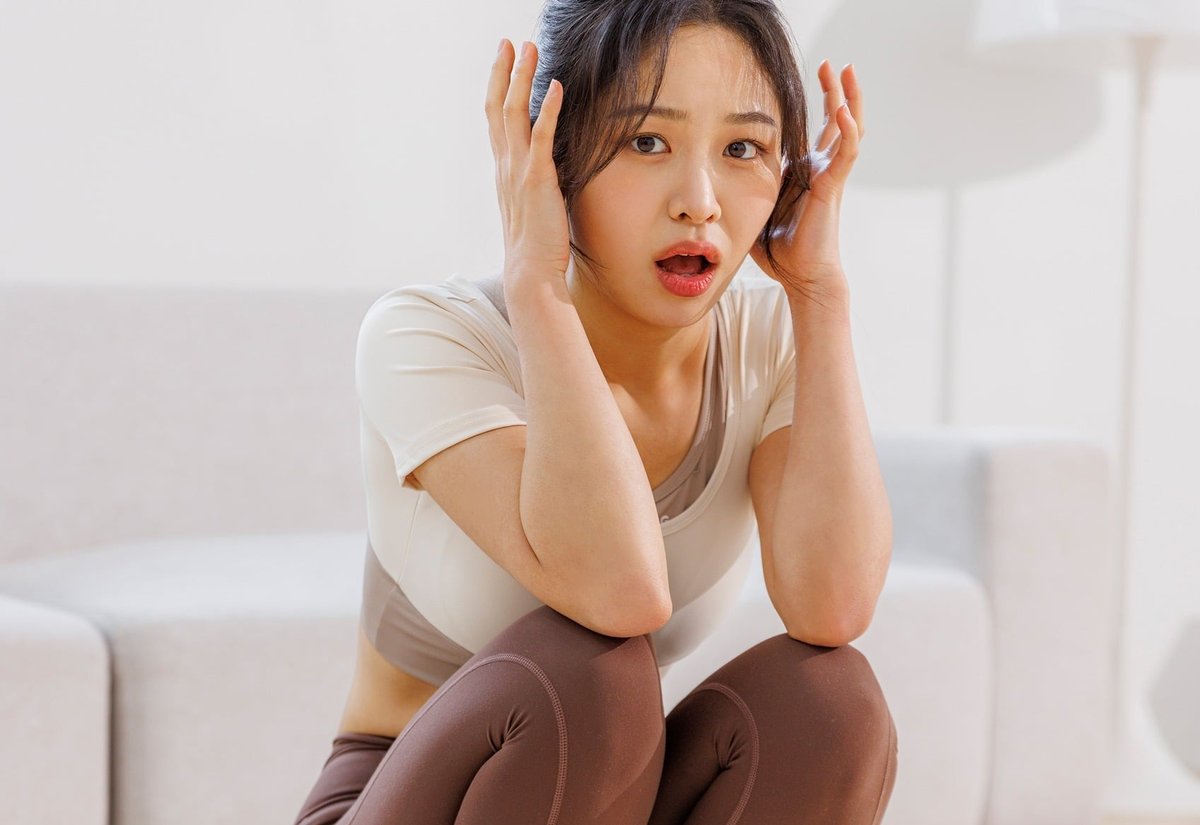 체중계 위에 쪼그려 앉아 두 손으로 머리를 감싸고 놀란 표정을 짓는 여성